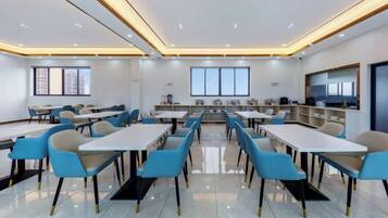 Una sala de conferencias moderna con mesas, sillas, una zona de cocina y un gran ventanal.