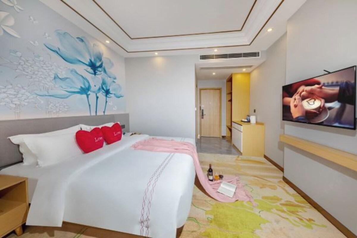A hotel room with a bed, a TV, a painting, and a desk.