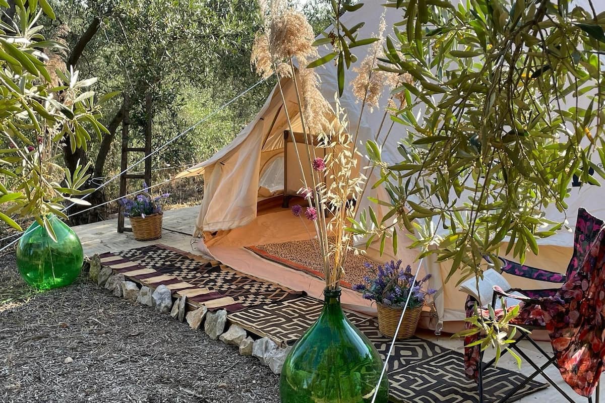A tent set up in a garden with a patterned rug, a green bottle, and a chair.