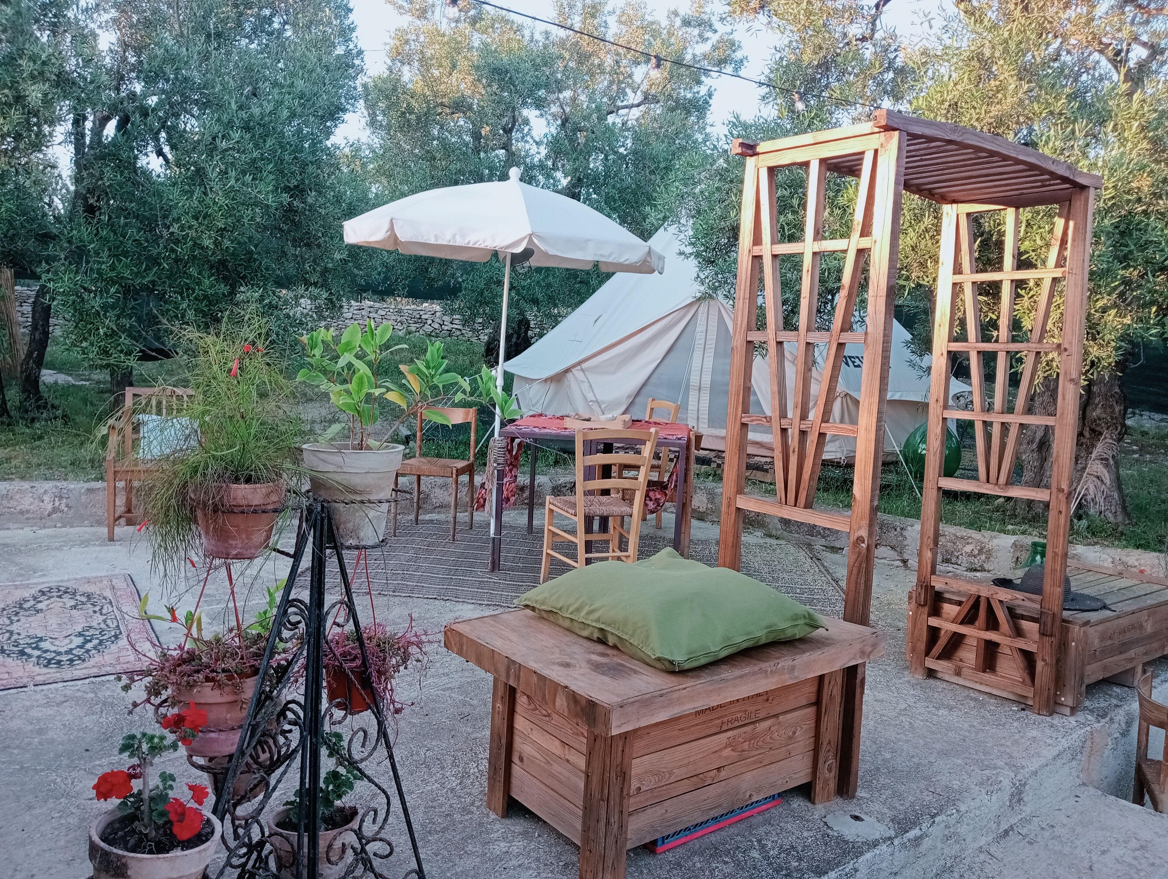 Un espace extérieur aménagé dans un style rustique, avec des meubles en bois, un parasol blanc et des plantes en pot.