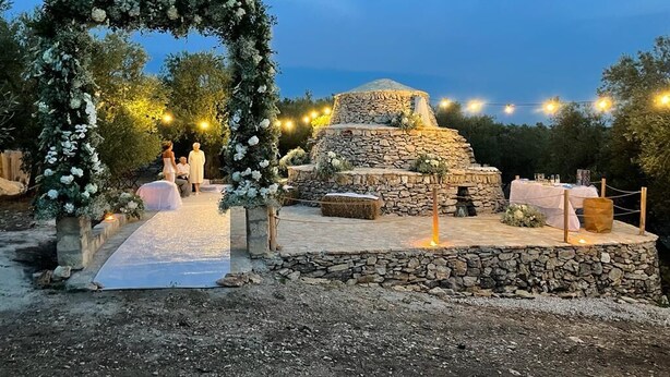 Decoración de boda al aire libre con una estructura de piedra, arco floral e iluminación con guirnaldas.