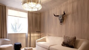 Ein modernes Wohnzimmer mit einem beigefarbenen Sofa, einem runden Hocker und einer Kristallleuchtre. An der Wand ist ein Bullskull als Dekoration angebracht.