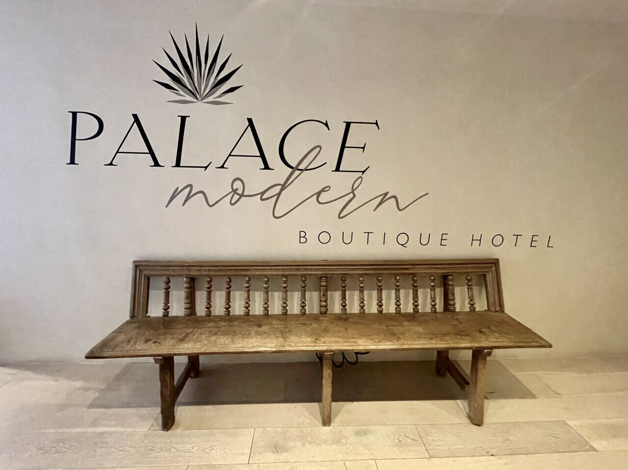 Un banc en bois devant un mur sur lequel on peut lire : « PALACE, hôtel-boutique moderne ».