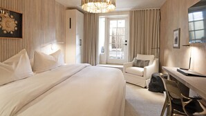 A hotel room with a large bed, a desk, a chair, a desk lamp, and a chandelier. - Palace Modern Hotel at the Plaza - Patio King 10 (Santa Fe)