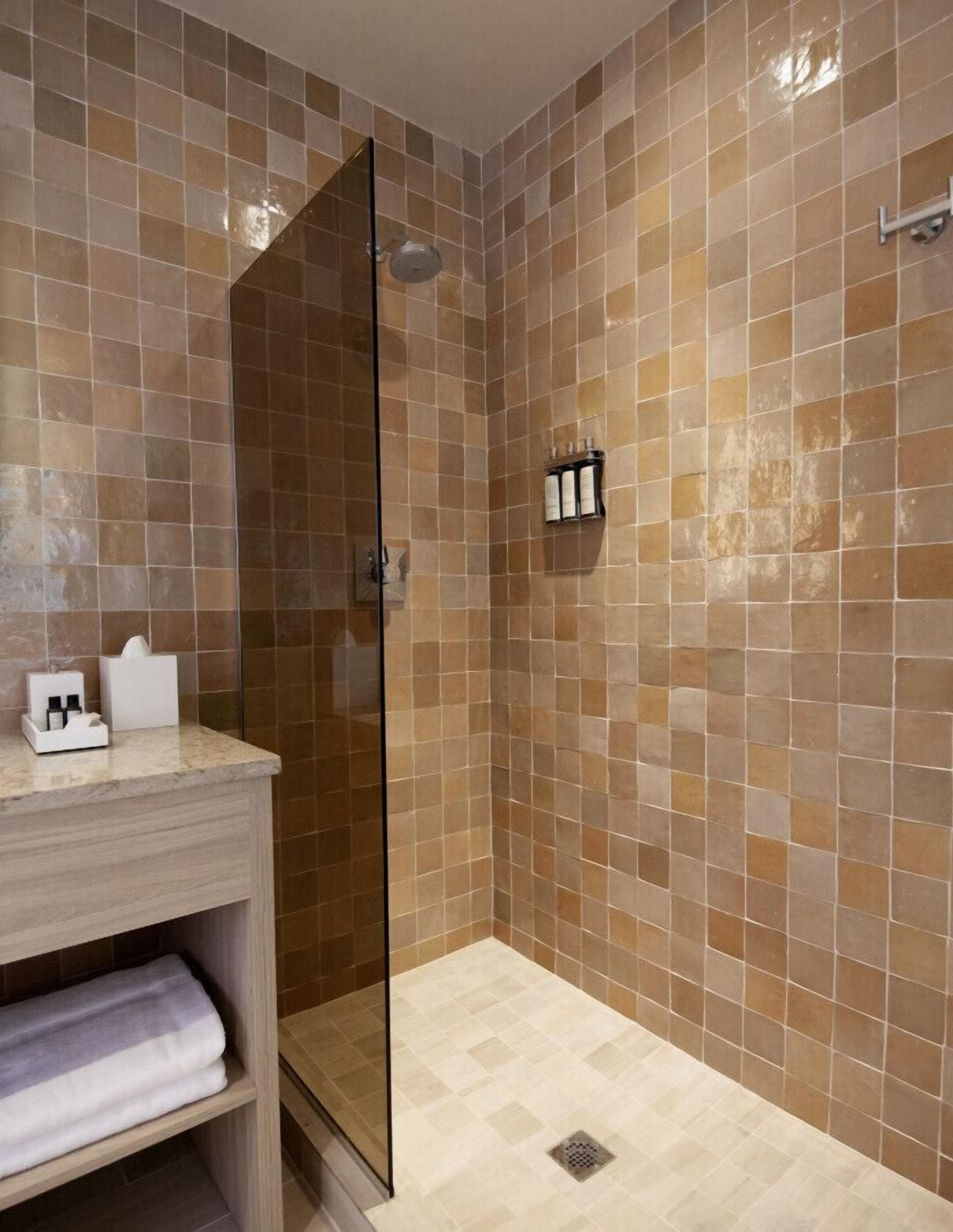 Un baño con cabina de ducha de vidrio, paredes con azulejos y un mueble de tocador de madera con estante para toallas.