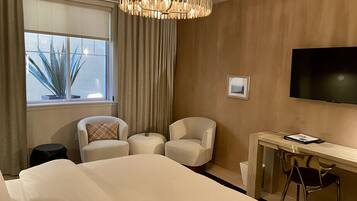 Una habitación de hotel con una cama grande, dos sillones, un escritorio y un televisor.