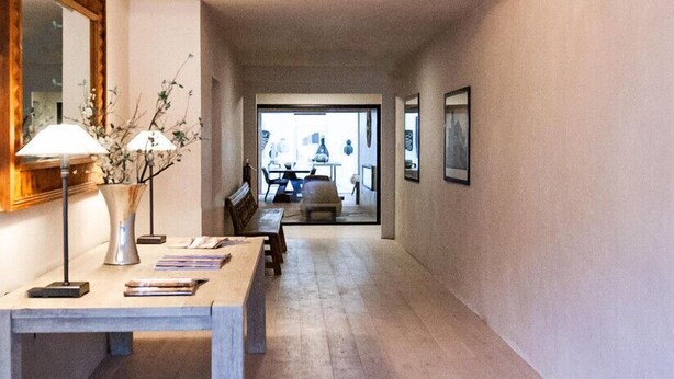 Un corridoio con un lampadario, un tavolo con libri, un vaso con fiori e quadri appesi al muro.