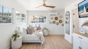 Ein modernes Schlafzimmer mit Bett, Deckenventilator, Fernseher und Blick auf die Stadt durch große Fenster.