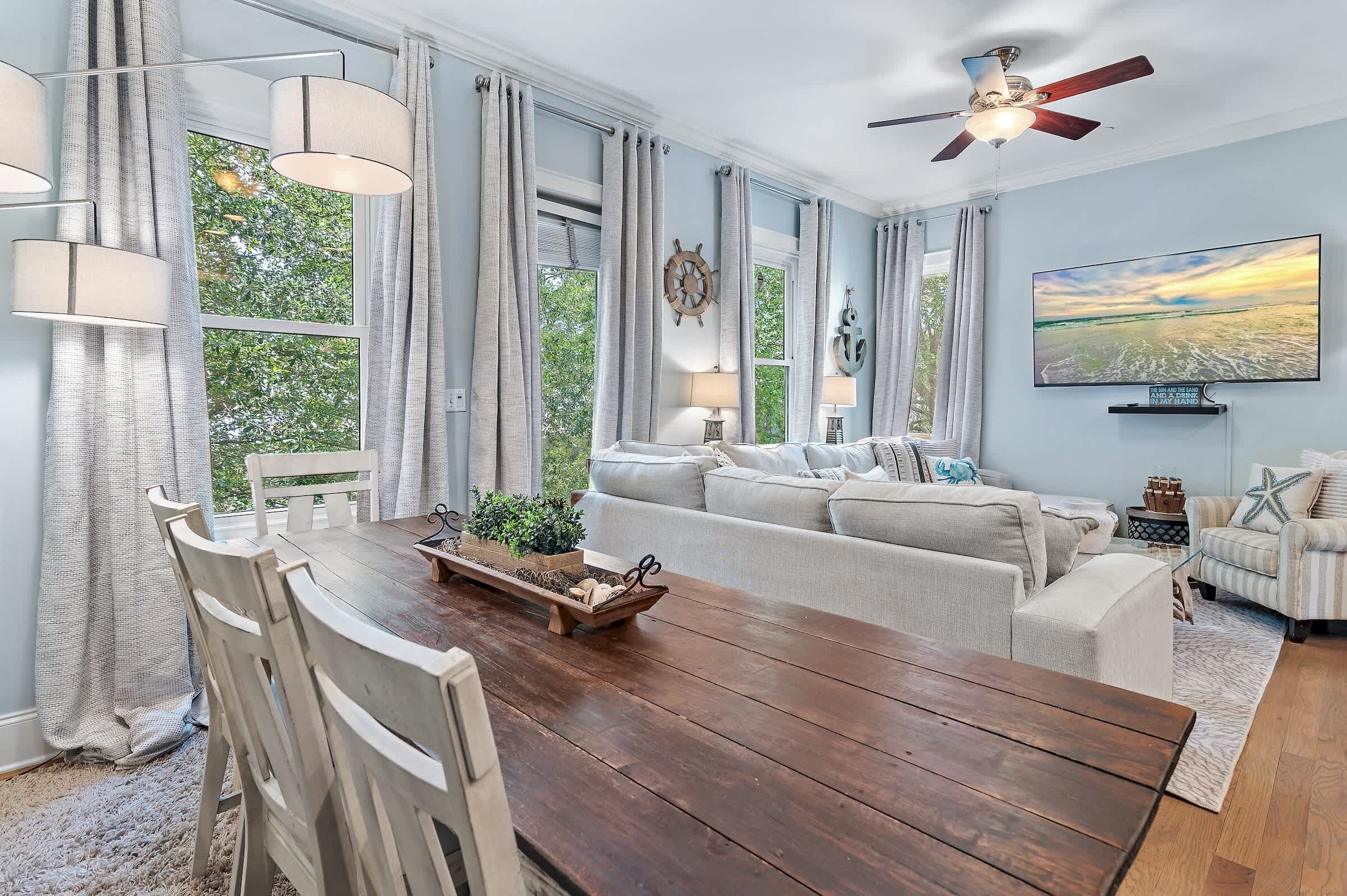A dining area with a wooden table, white chairs, and a view of greenery outside.