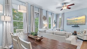 A dining area with a wooden table, white chairs, and a view of greenery outside. - 30A Rooftop Retreat | Heated Pool Escape (Santa Rosa Beach)
