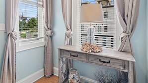 A room with a light blue wall, a wooden console table with drawers, a decorative lamp, and a window with blinds and curtains. - 30A Rooftop Retreat | Heated Pool Escape (Santa Rosa Beach)