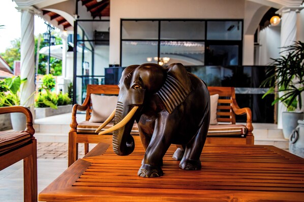 A wooden elephant statue on a bench in an outdoor seating area with wooden chairs and a potted plant. - Paradise Holiday Village (Negombo)