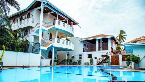 A large swimming pool with a multi-level building in the background. - Paradise Holiday Village (Negombo)