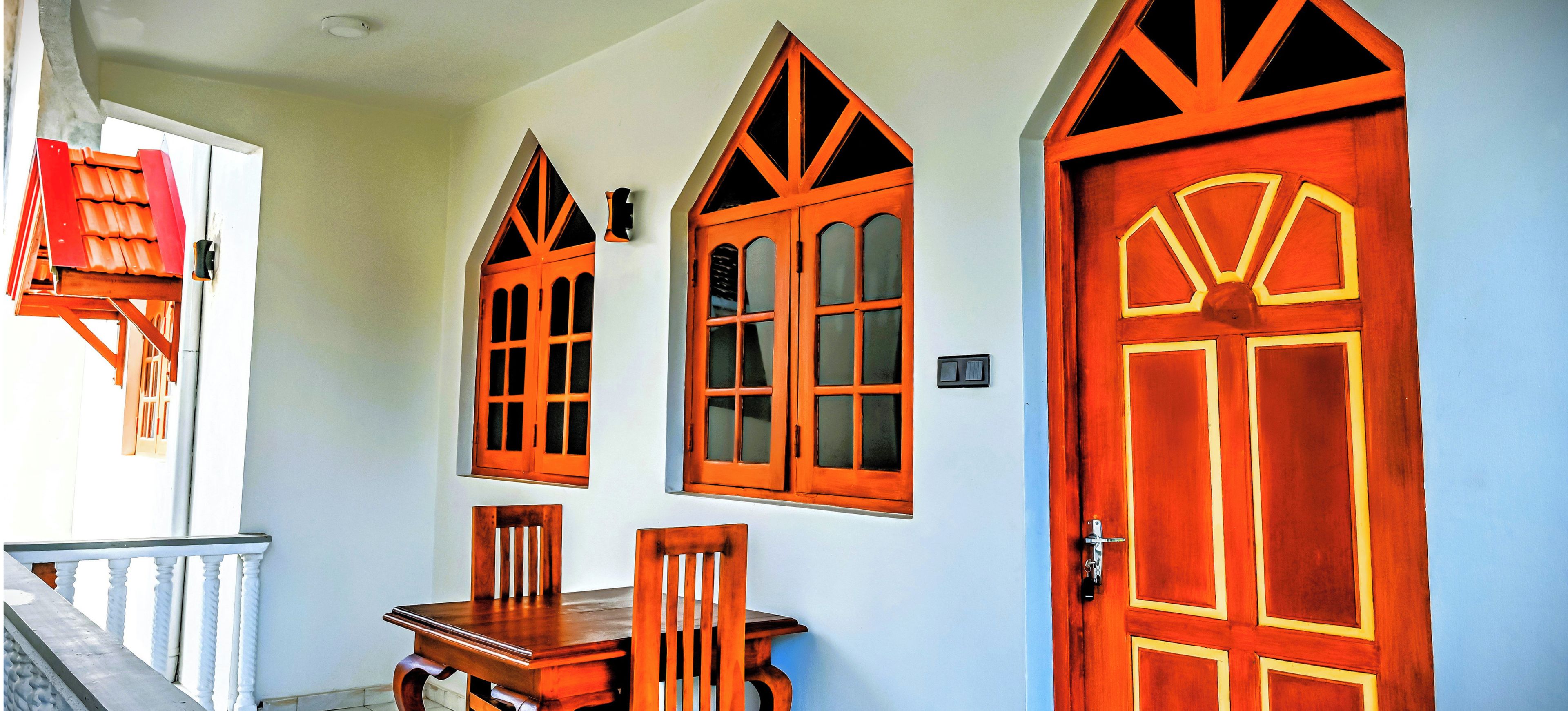 A hallway with a wooden table and chairs, a red door, and a window with a red frame.