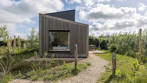 Un bâtiment moderne et minimaliste, doté d’une grande fenêtre, entouré d’un chemin de gravier et de verdure.