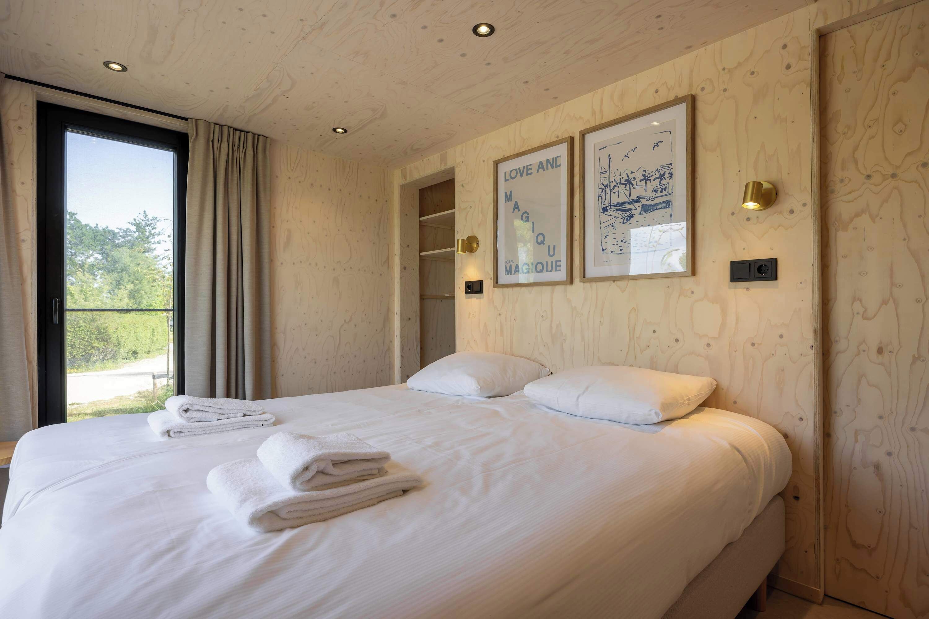 Una camera da letto con un letto grande, una finestra con tende, un muro in legno e due quadri appesi.
