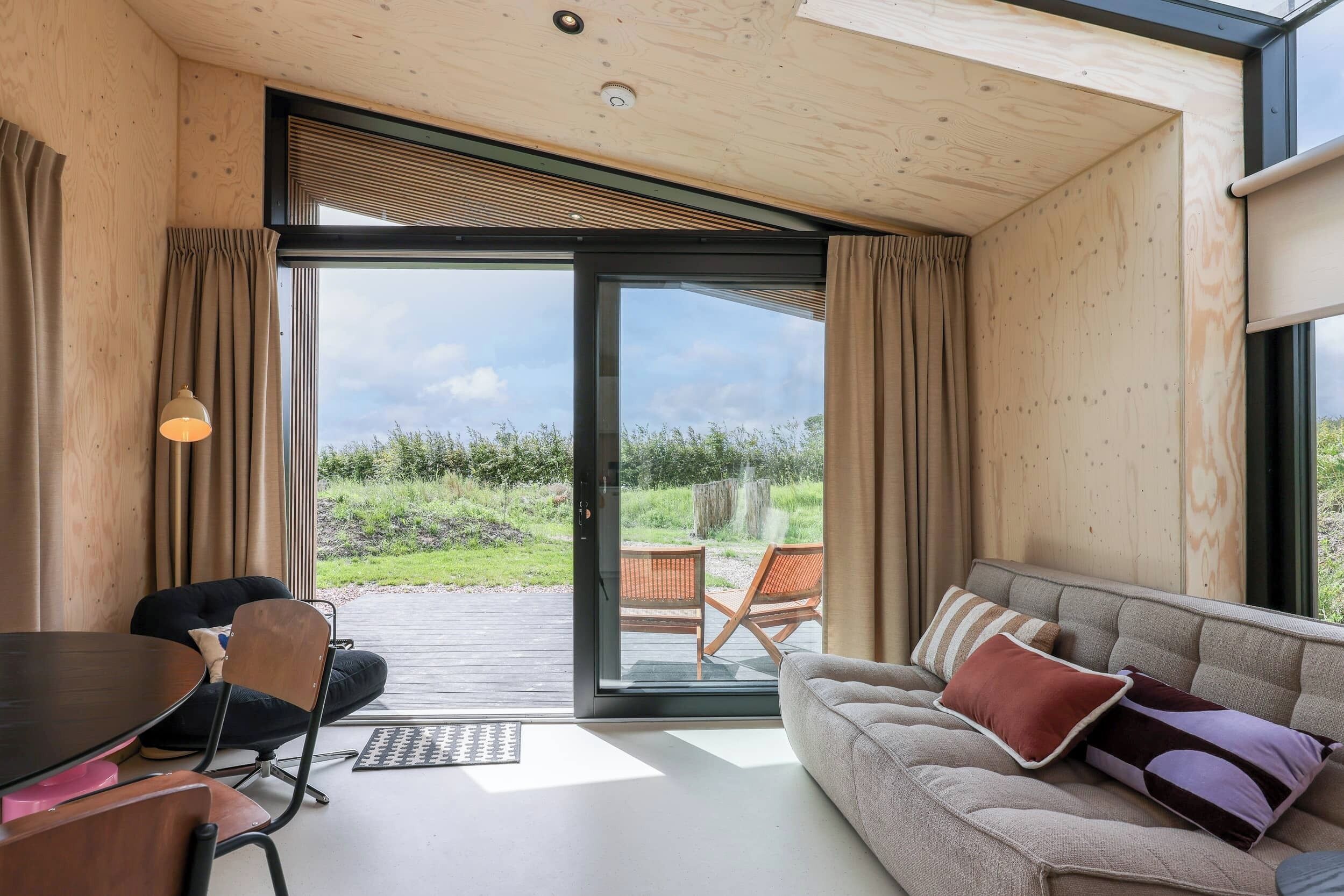 A modern interior with a wooden ceiling, a sofa with cushions, a dining table, and a sliding glass door leading to an outdoor seating area.