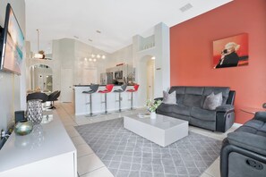 A modern living room with a grey sofa, a white coffee table, and a kitchen in the background. - Charming 4BR home w/ pool & hot tub (Kissimmee)