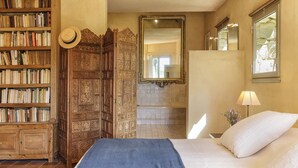 A bedroom with a bed, a bookshelf, a wooden wardrobe, a mirror, and a bathroom visible through an open door. - Fabulous houses with breathtaking views in a peaceful and stunning environment (Suzette)