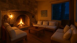 A cozy living room with a stone fireplace, a sofa, a coffee table, and a large window with a view of trees. - Fabulous houses with breathtaking views in a peaceful and stunning environment (Suzette)