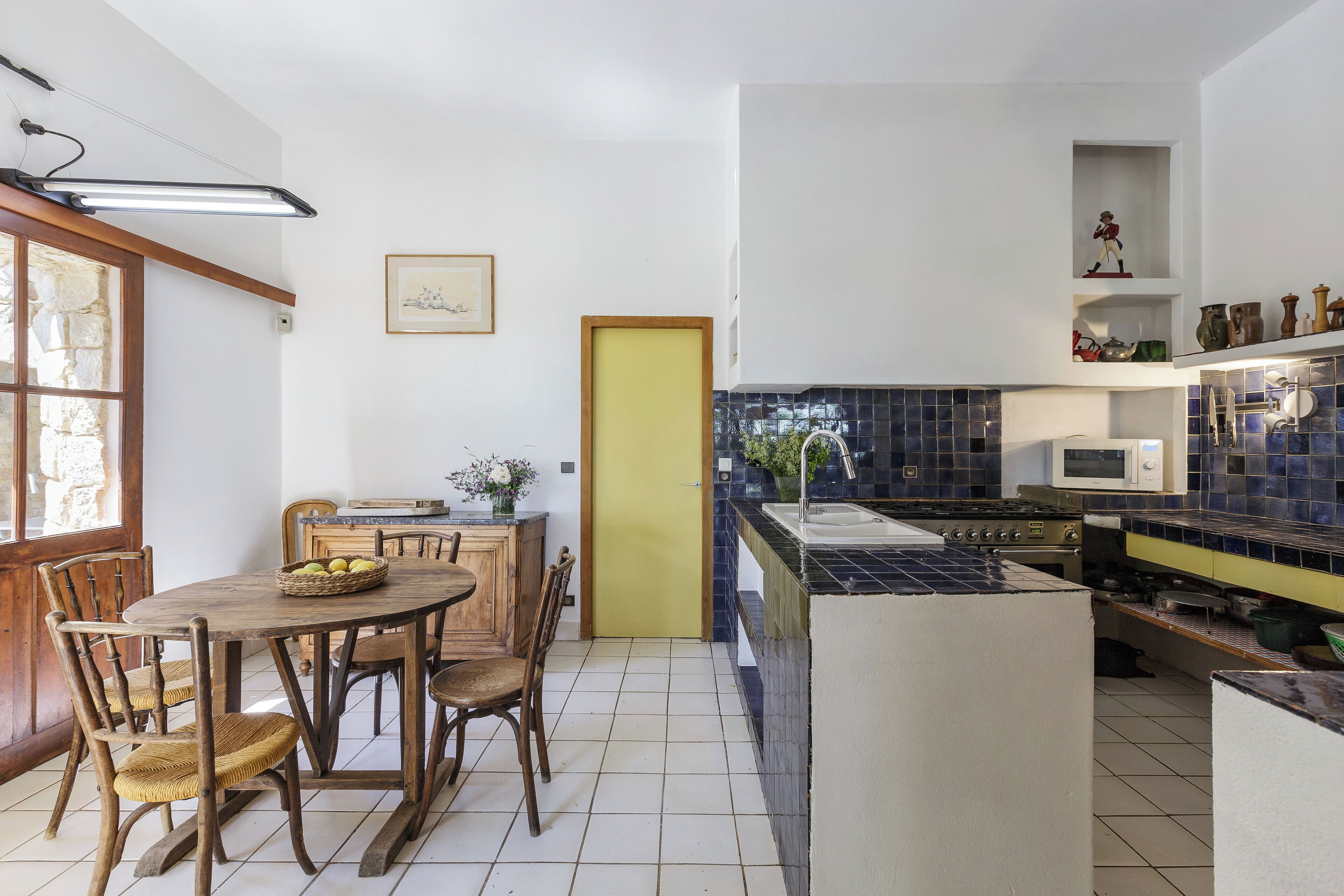 Une cuisine avec une table à manger, des chaises, une porte jaune et un mur recouvert de carreaux.