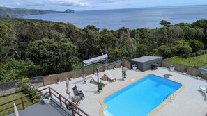 Zona de piscina con sillones reclinables, una pequeña terraza y vistas al océano.