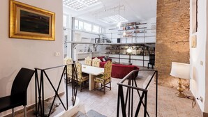 A dining area with a table and chairs, a red sofa, and a bookshelf filled with books. - Navona Glamour Apartment (Rome)
