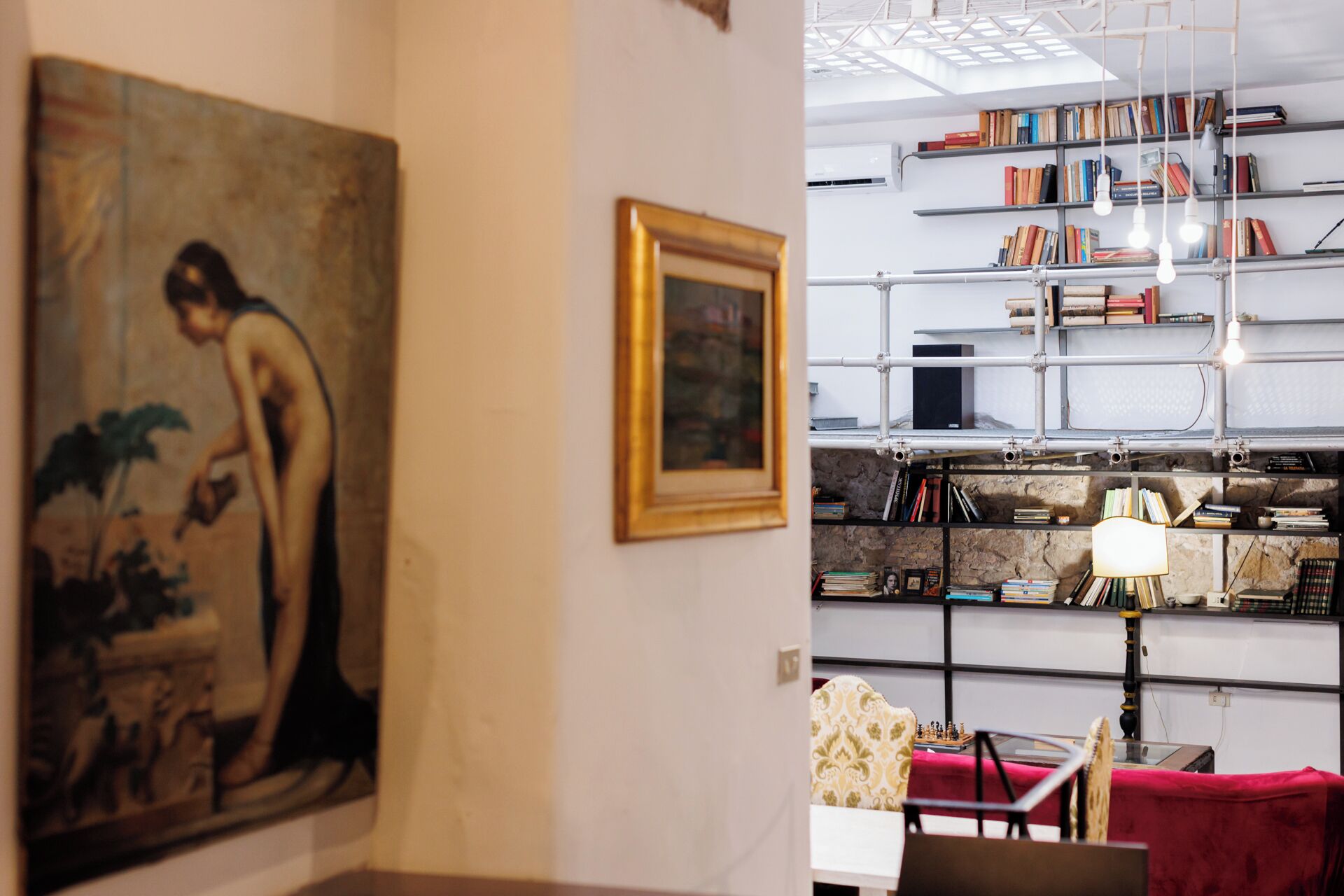 A room with a painting, a framed picture, a bookshelf, and a chessboard.