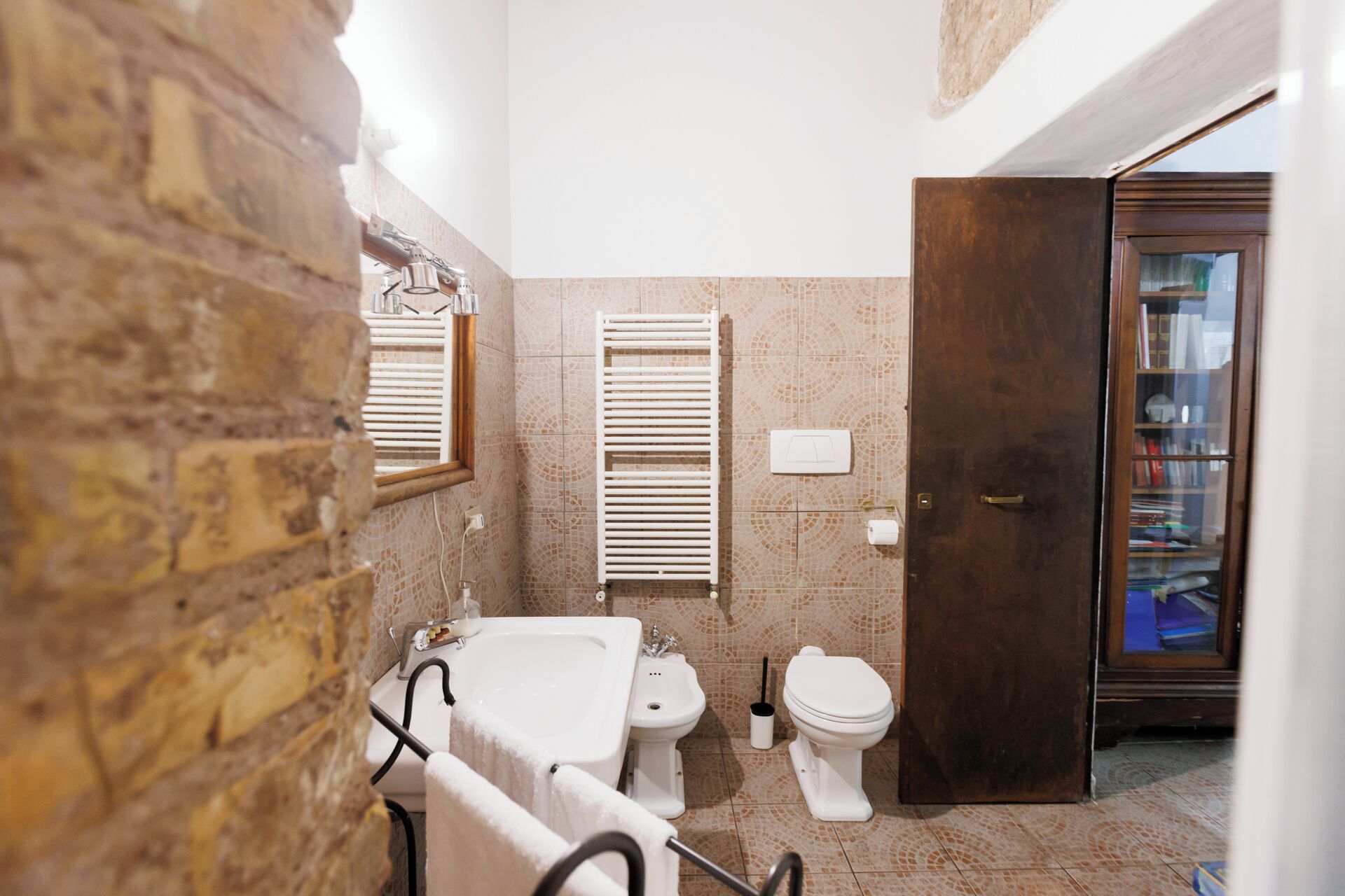 A bathroom with a bathtub, a toilet, and a shower. There is a towel rack with towels, a window with blinds, and a door leading to another room.