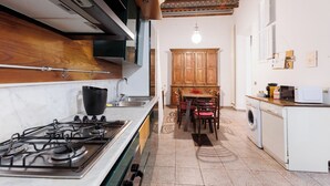 A compact kitchen with a gas stove, wooden cabinets, and a dining area with chairs. - Navona Glamour Apartment (Rome)