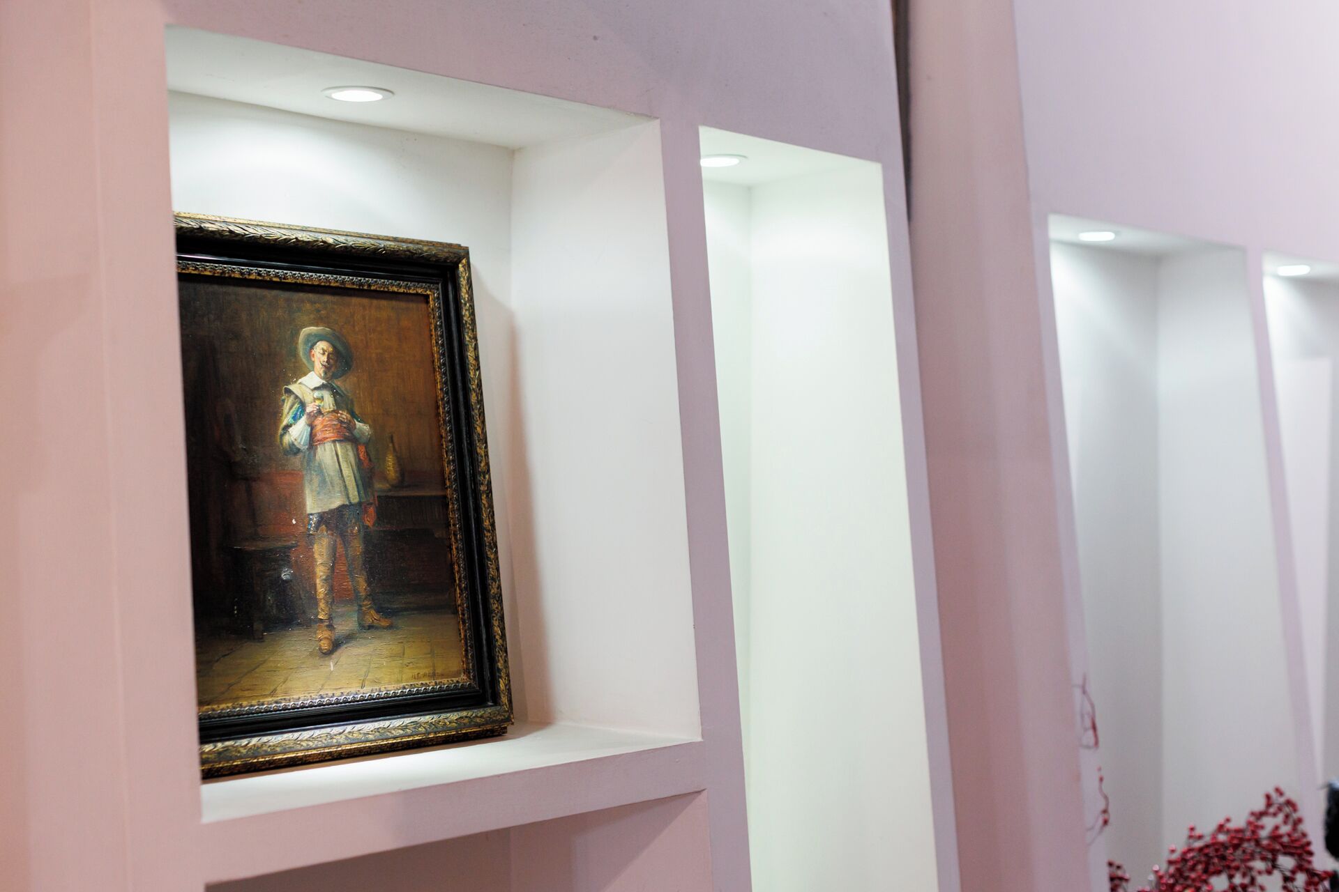 A framed artwork in a display case, with a white wall and a pinkish hue in the background.