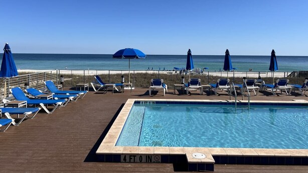 A poolside area with blue umbrellas and lounge chairs, a clear view of the ocean, and a sign indicating the pool depth. - 3 br, gulf view, beach club, pools, gym, hot tub (Pensacola)