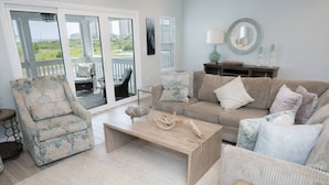 A living room with a sofa, armchair, and coffee table. There is a sliding glass door leading to a balcony. - 3 br, gulf view, beach club, pools, gym, hot tub (Pensacola)