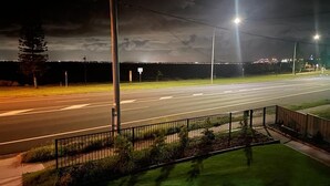 A nighttime view of a road with streetlights, a grassy area, and a fence. - Beach View Cottage. Cosy with direct water views. (Clontarf)