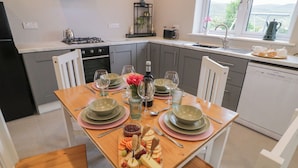 A modern kitchen with a dining table set for four, featuring a fruit platter, wine glasses, and plates. - ARD NA GHAOITHE, pet friendly in Loughanure, County Donegal (Loughanure)