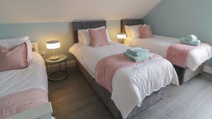 A bedroom with two beds, each with a bedside table and lamp, and a small round table in the center. - ARD NA GHAOITHE, pet friendly in Loughanure, County Donegal (Loughanure)