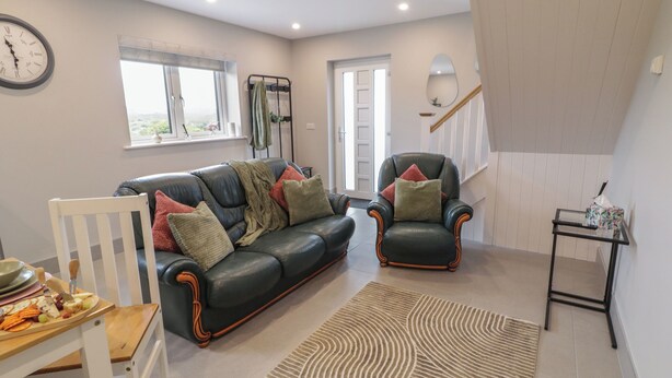 A living room with a leather sofa, a wooden chair, a small table with a cheese board, a patterned rug, a clock, and a staircase. - ARD NA GHAOITHE, pet friendly in Loughanure, County Donegal (Loughanure)
