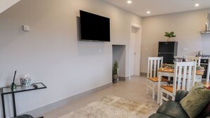 A modern living room with a flat-screen TV mounted on the wall, a dining area with a table and chairs, and a kitchen in the background. - ARD NA GHAOITHE, pet friendly in Loughanure, County Donegal (Loughanure)