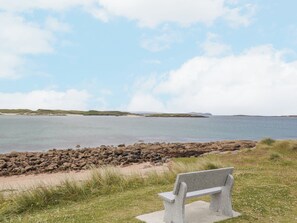 A bench by a rocky shoreline with a view of the sea and distant land.
