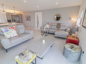 A modern living room with a grey sofa, a matching armchair, a coffee table, and a round ottoman with floral upholstery. A small side table with a lamp is also visible. - COTTAGE CATRIONA, family friendly in Derrybeg, County Donegal (.)