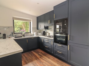 A modern kitchen with dark cabinetry, a built-in oven, and a window with a view of greenery.