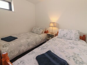 A bedroom with two single beds, a bedside table with a lamp, and a window.