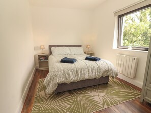 A bedroom with a bed, two bedside tables, a window, and a radiator.