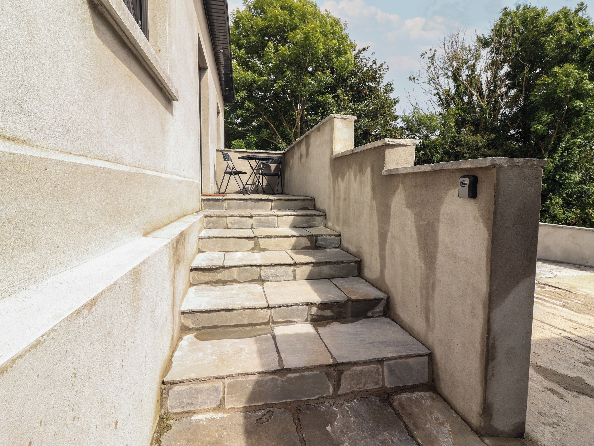 A set of stone steps leading up to a building entrance, with a small table and chairs nearby.