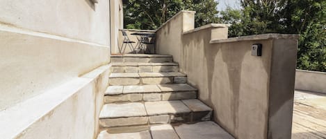 A set of stone steps leading up to a building entrance, with a small table and chairs nearby.