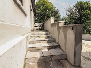 Degraus de pedra que levam à entrada de um edifício, com uma pequena mesa e cadeiras por perto.