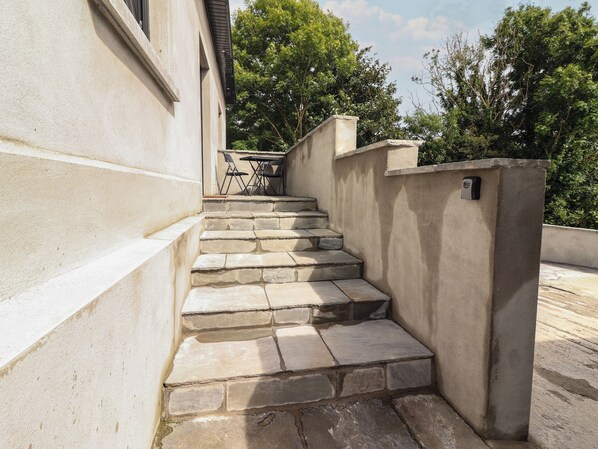 A set of stone steps leading up to a building entrance, with a small table and chairs nearby.