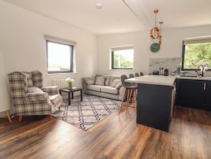 A modern living room with a sofa, a plaid armchair, a coffee table, and a dining area with bar stools.