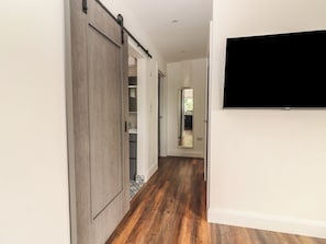 A hallway with a wooden floor, a sliding door, a mirror, and a mounted TV.