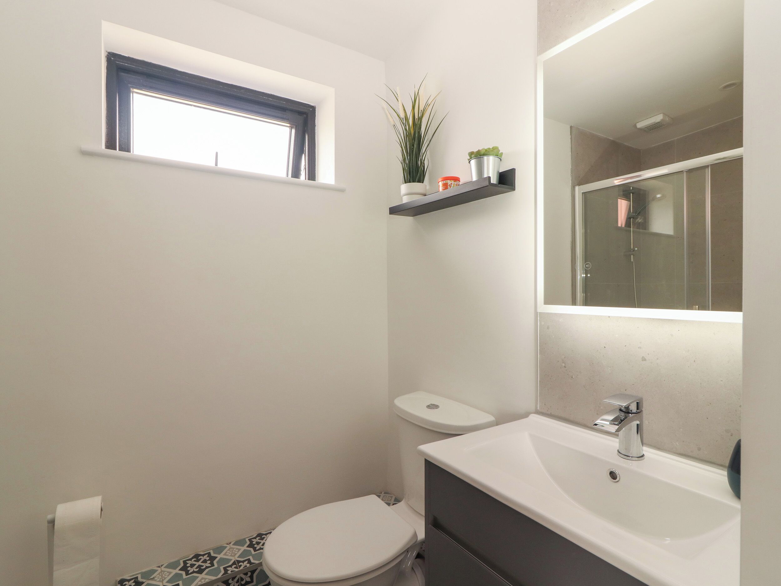 Ein Badezimmer mit Toilette, Waschbecken, Spiegel und kleinem Fenster.